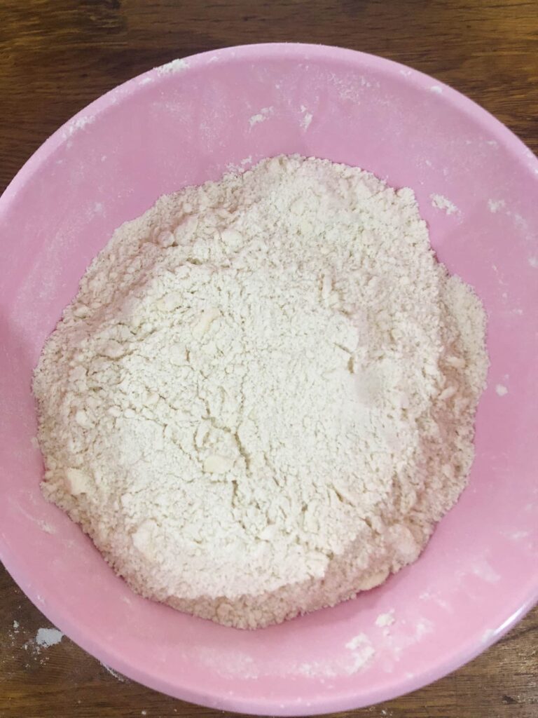 pink bowl filled with flour salt and butter which has been rubbed together to form breadcrumbs