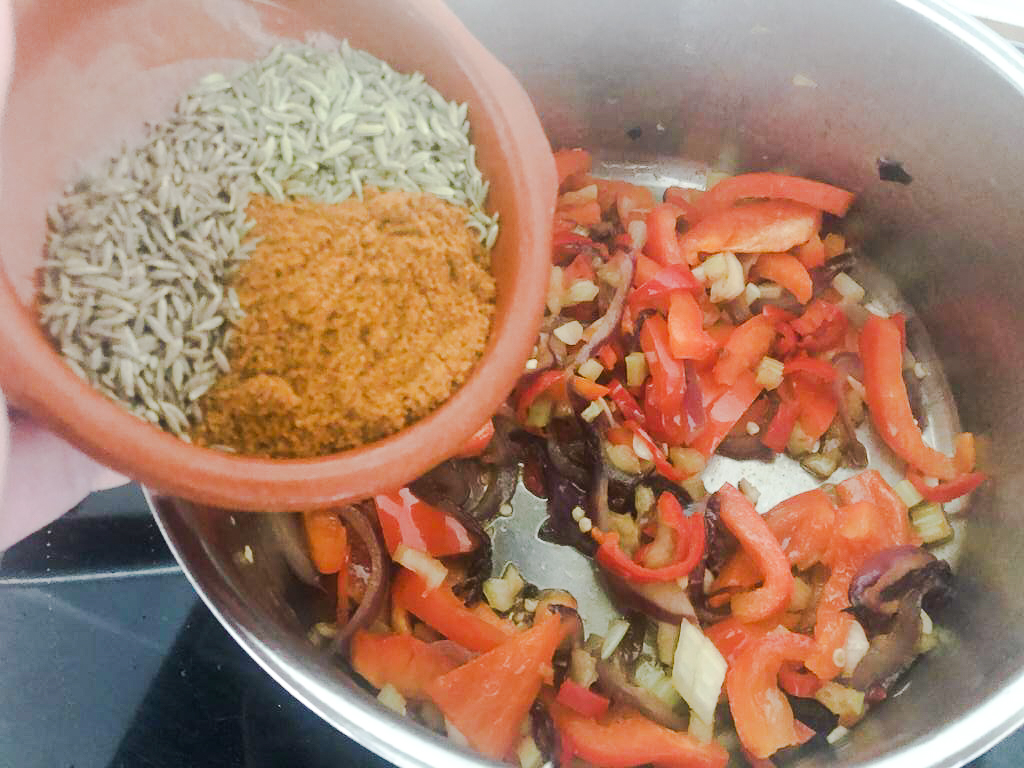 saucepan with sauteed vegetables and dish with spices being added