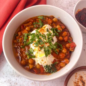 white bowl filled with Moroccan chickpea stew topped with a spoon of Greek yogurt, freshly chopped mind and a drizzle of olive oil