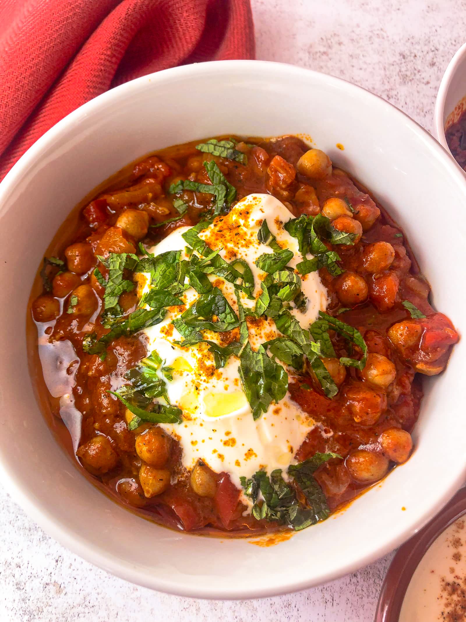 white bowl filled with Moroccan chickpea stew topped with a spoon of Greek yogurt, freshly chopped mind and a drizzle of olive oil