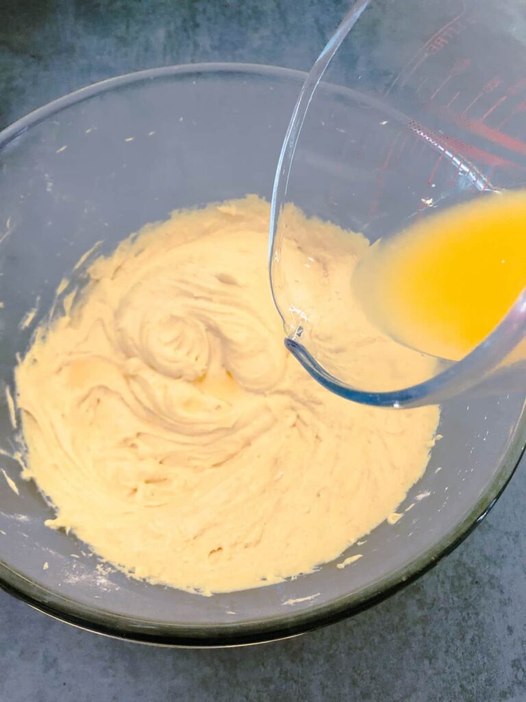 glass bowl of orange cake batter with fresh orange juice being added