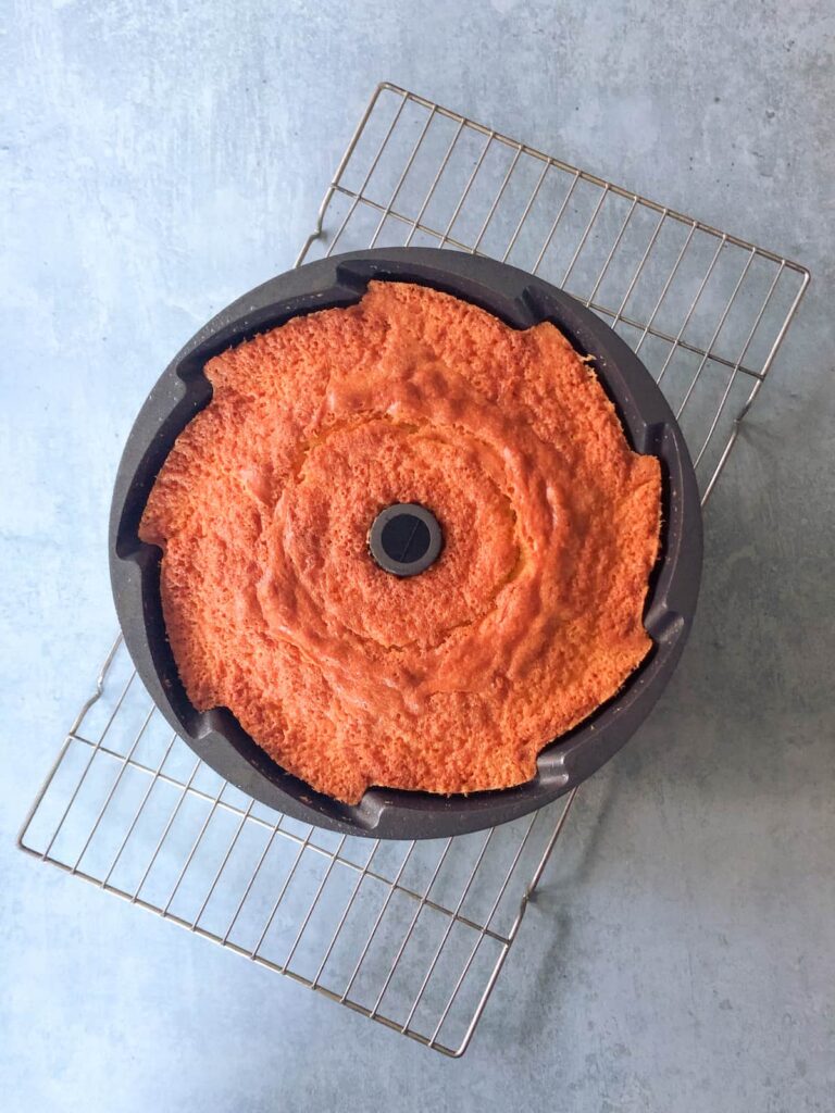 baked orange cake in bundt tin resting on a wire cooling rack