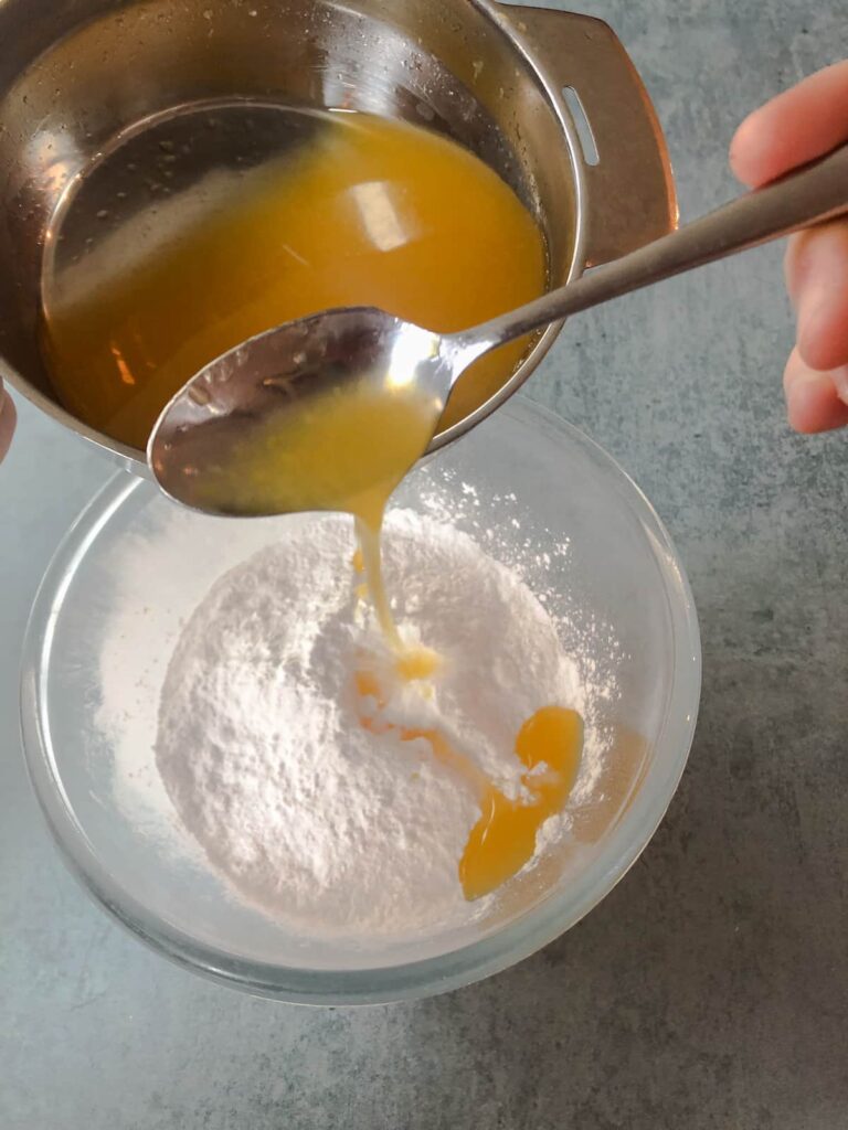 glass bowl filled with icing sugar and teaspoons of fresh orange juice being added