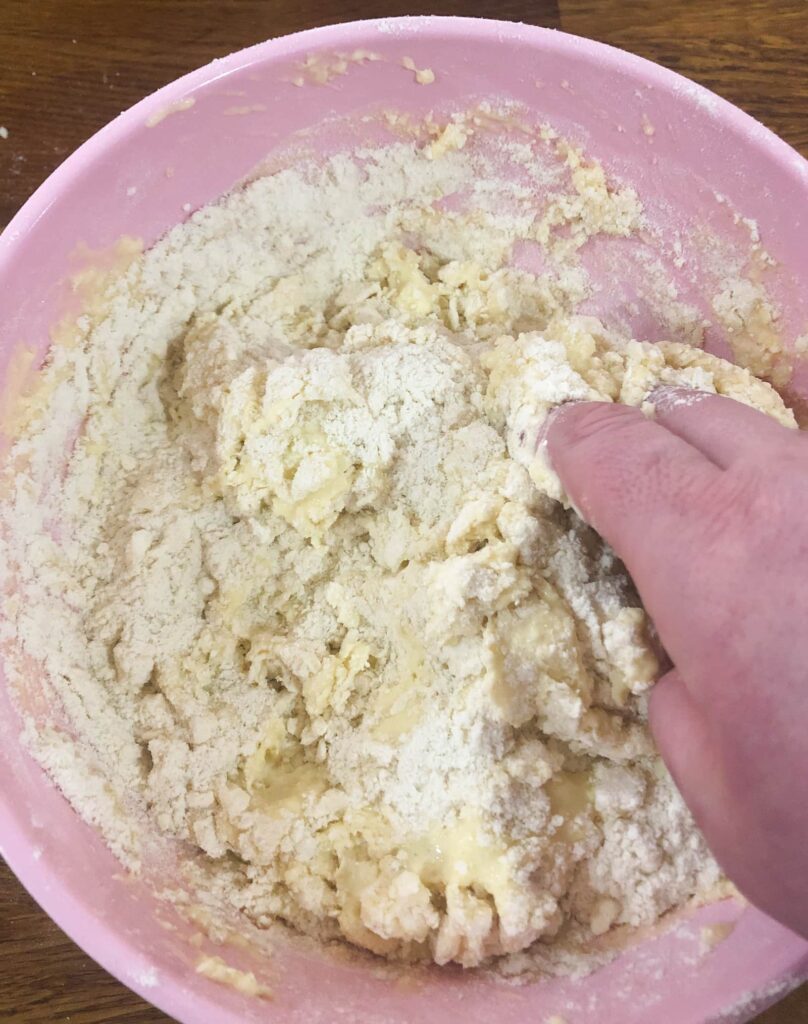 pink bowl with combined wet and dry ingredients for scones, being brought together by hand to form a ball of dough