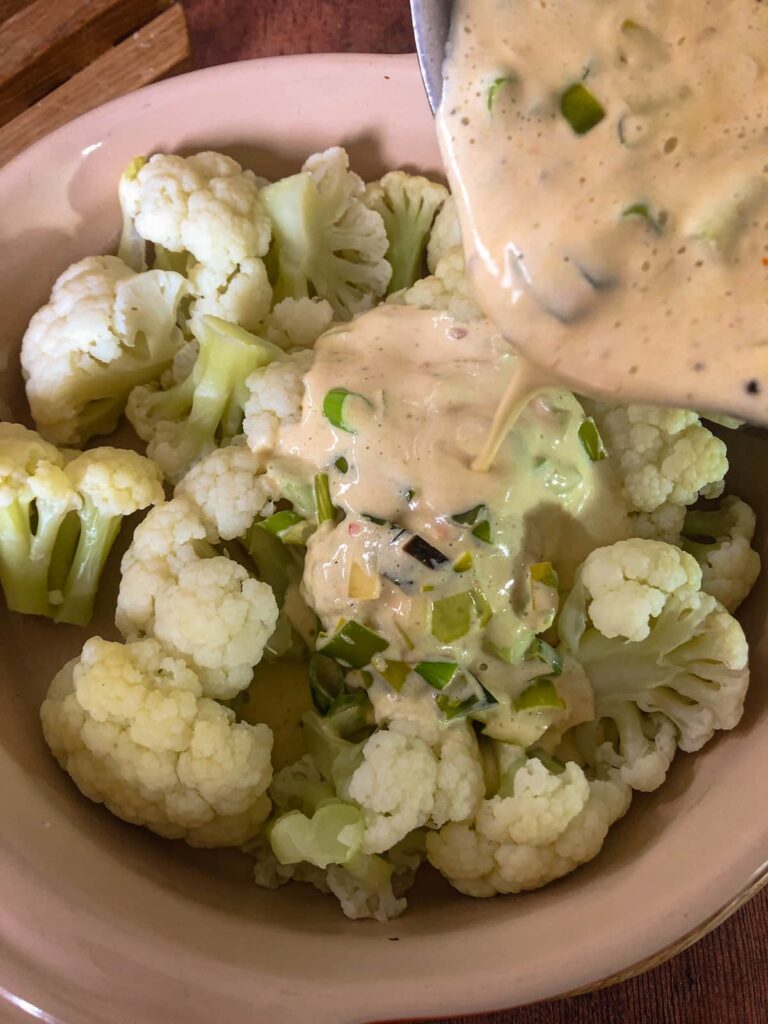 oven proof dish filled with florets of cooked cauliflower with a cheese and leek sauce being poured over