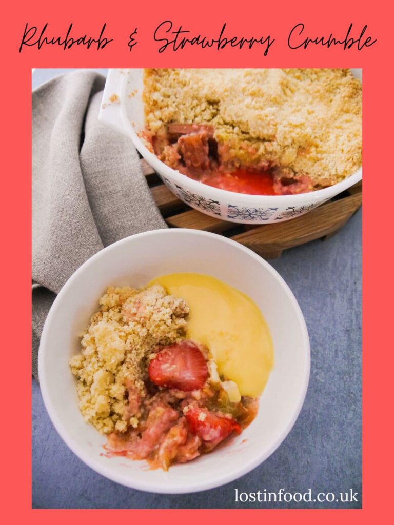 Pinnable image with recipe title and white pyrex dish filled with rhubarb and strawberry crumble, set on a wooden board, with a while bowl of crumble and custard set alongside.