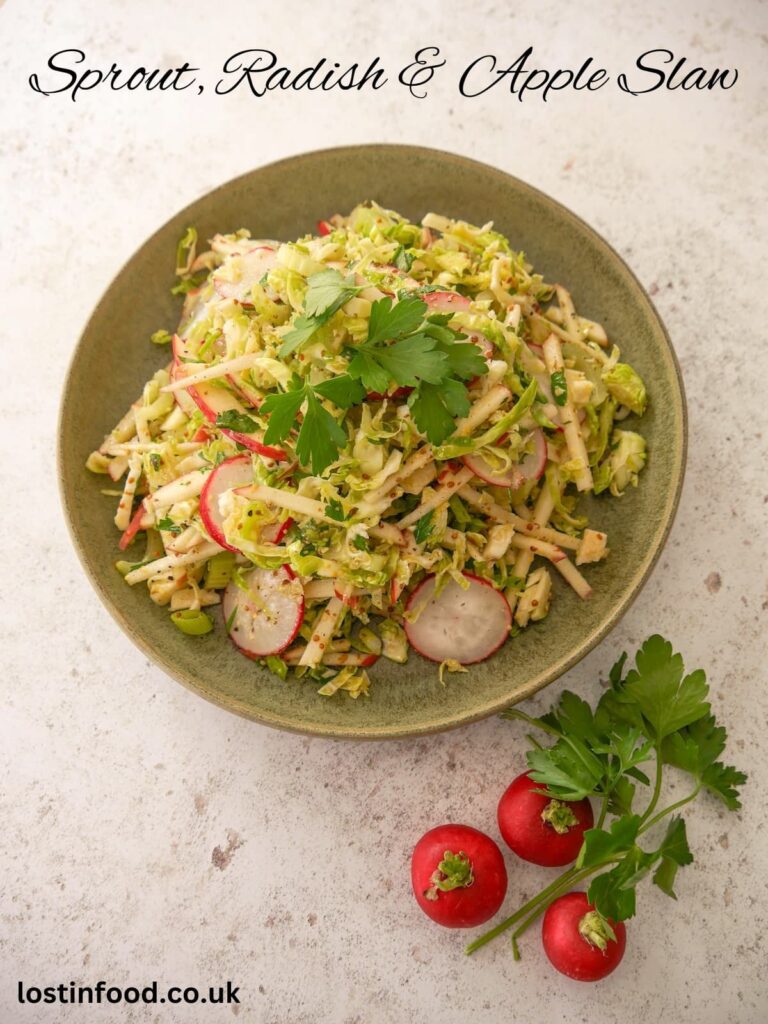 Pinnable image with recipe title and a green bowl filled with dressed shredded Brussels sprouts, red apple, celery and sliced radish, garnished with parsley and whole radishes and a sprig of parsley set alongside.