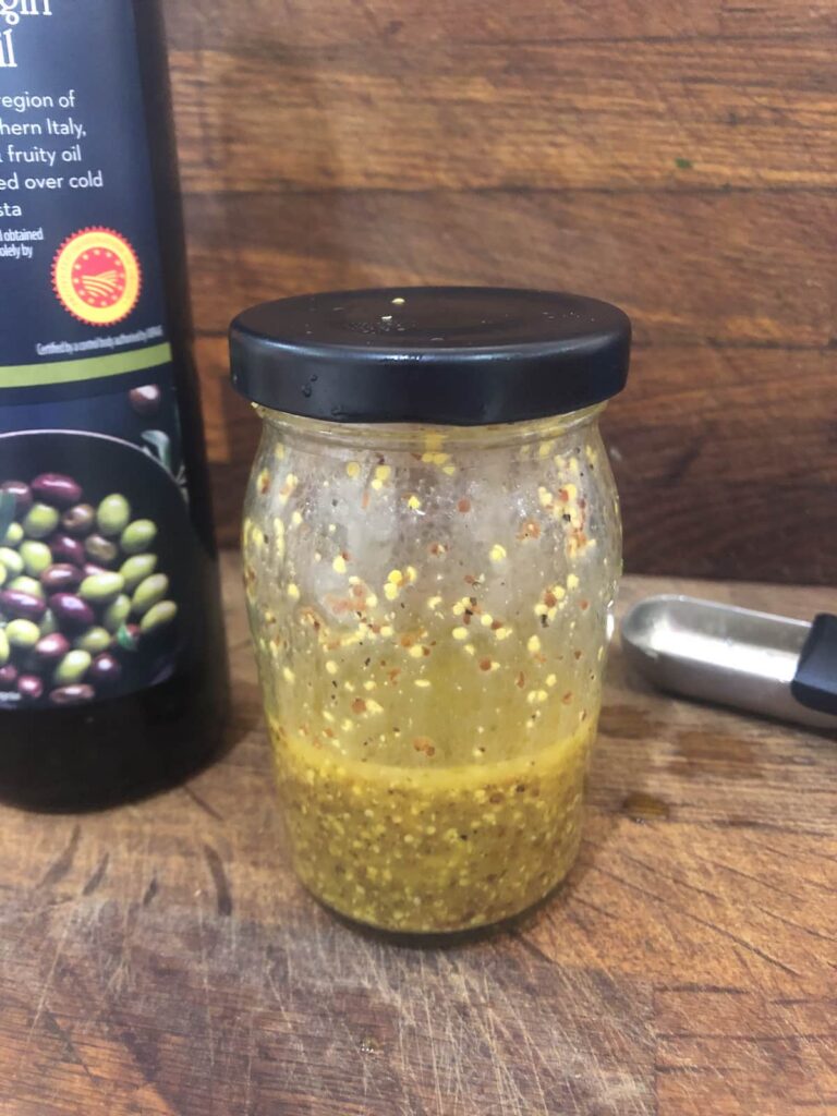 A jam jar filled with honey and mustard salad dressing and a bottle of olive oil set alongside.