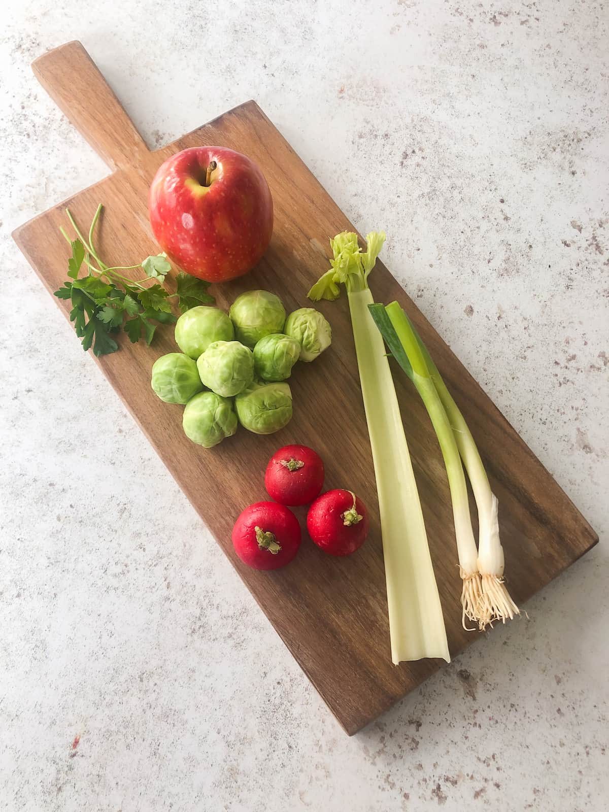Sprout and apple slaw recipe ingredients set onto a wooden board.