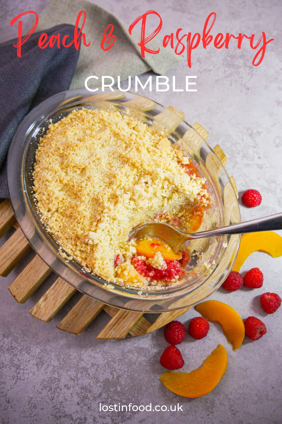 pinnable image with recipe title and glass dish of peach and raspberry crumble set onto a wooden trivet with a portion of crumble removed and fresh sliced peaches and raspberries set alongside