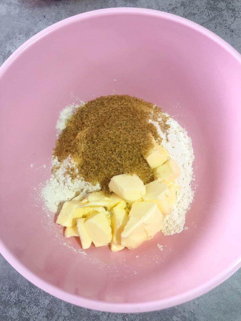 pink bowl filled with flour, demerara sugar and cubes of butter