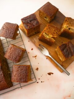 Rhubarb and ginger cake set on a wire rack with a wooden board topped with slices of cake set alongside.