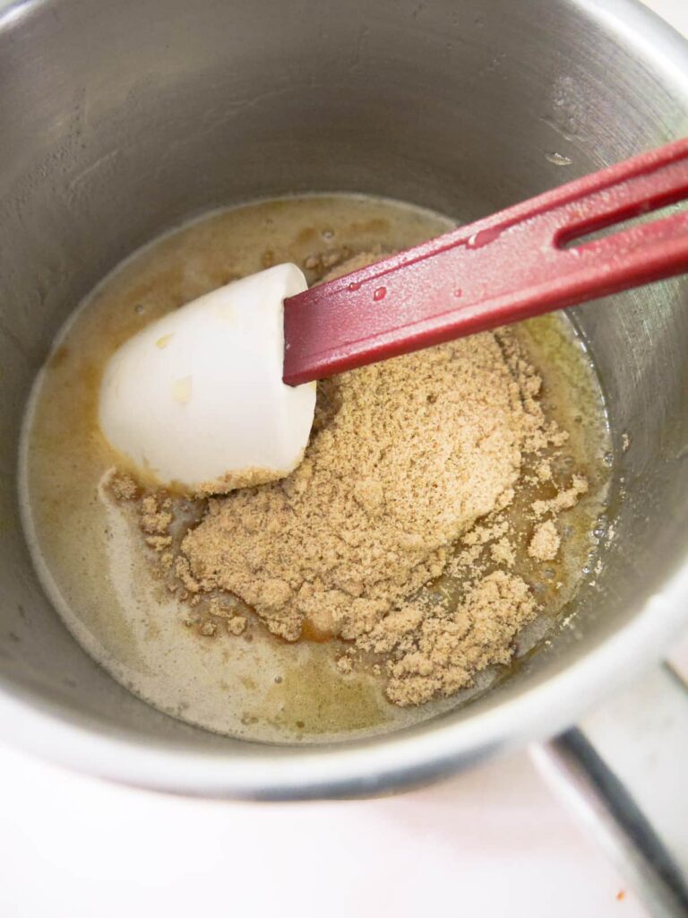 Brown muscovado sugar being stirred into a saucepan filled with melted honey and butter.