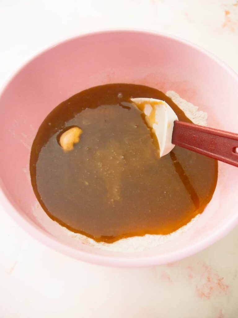 Pink bowl filled with flour and spices and melted butter, honey and sugar being stirred through.