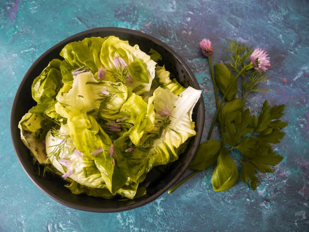 Black bowl filled with dressed lettuce and chopped herb salad with stems of fresh herbs alongside.