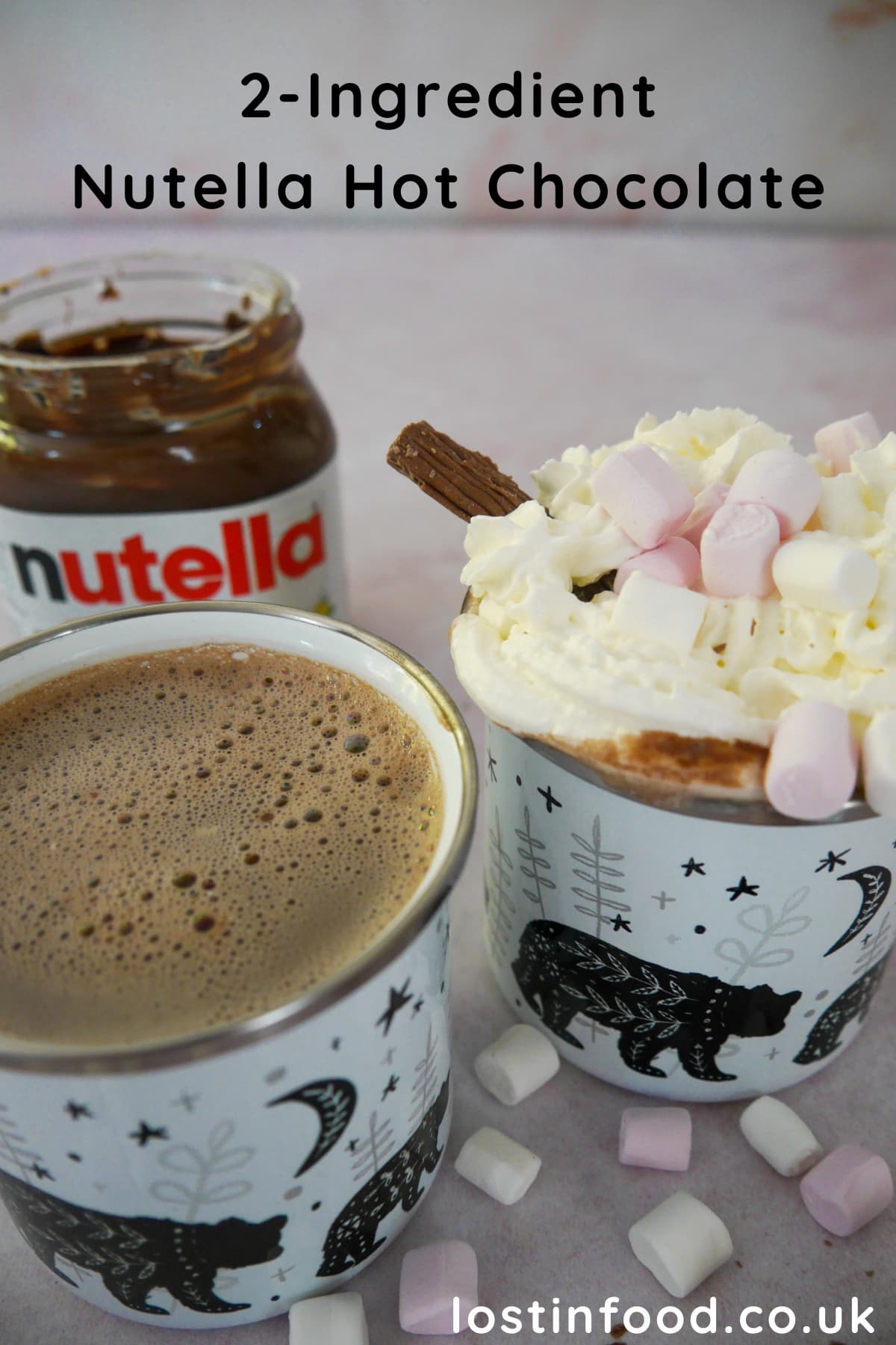 Pinnable image with two mugs of hot chocolate, one topped with whipped cream, mini marshmallows and a chocolate log, with an open jar of Nutella, mini marshmallows and chocolate logs set alongside.