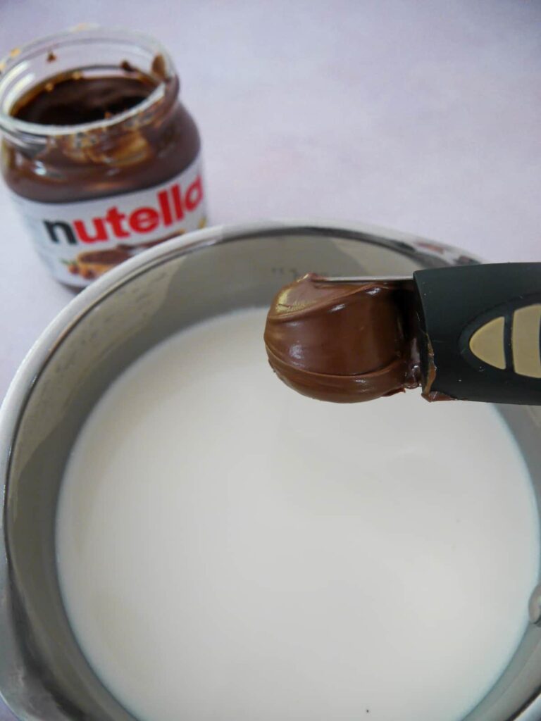 A saucepan of milk with a tablespoon of Nutella being added.