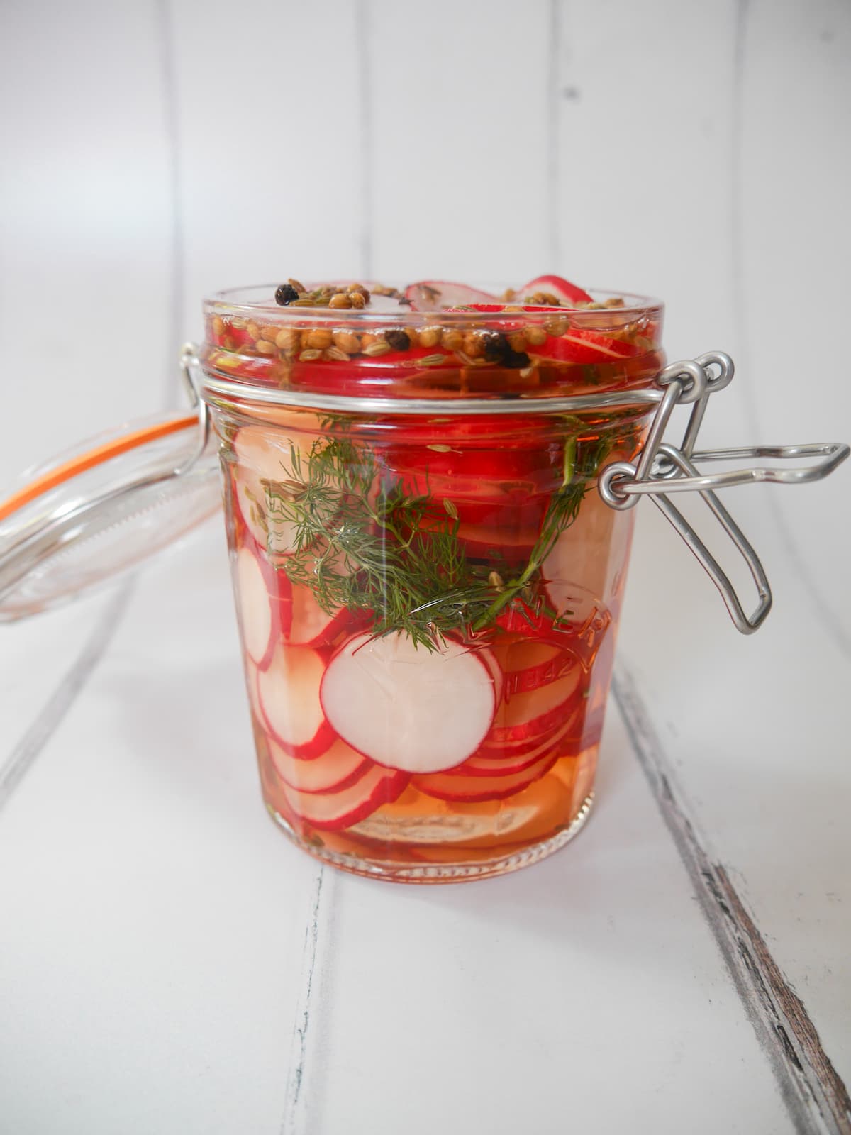 An open mason jar filled with pickled radish, dill fronds, and whole spices.