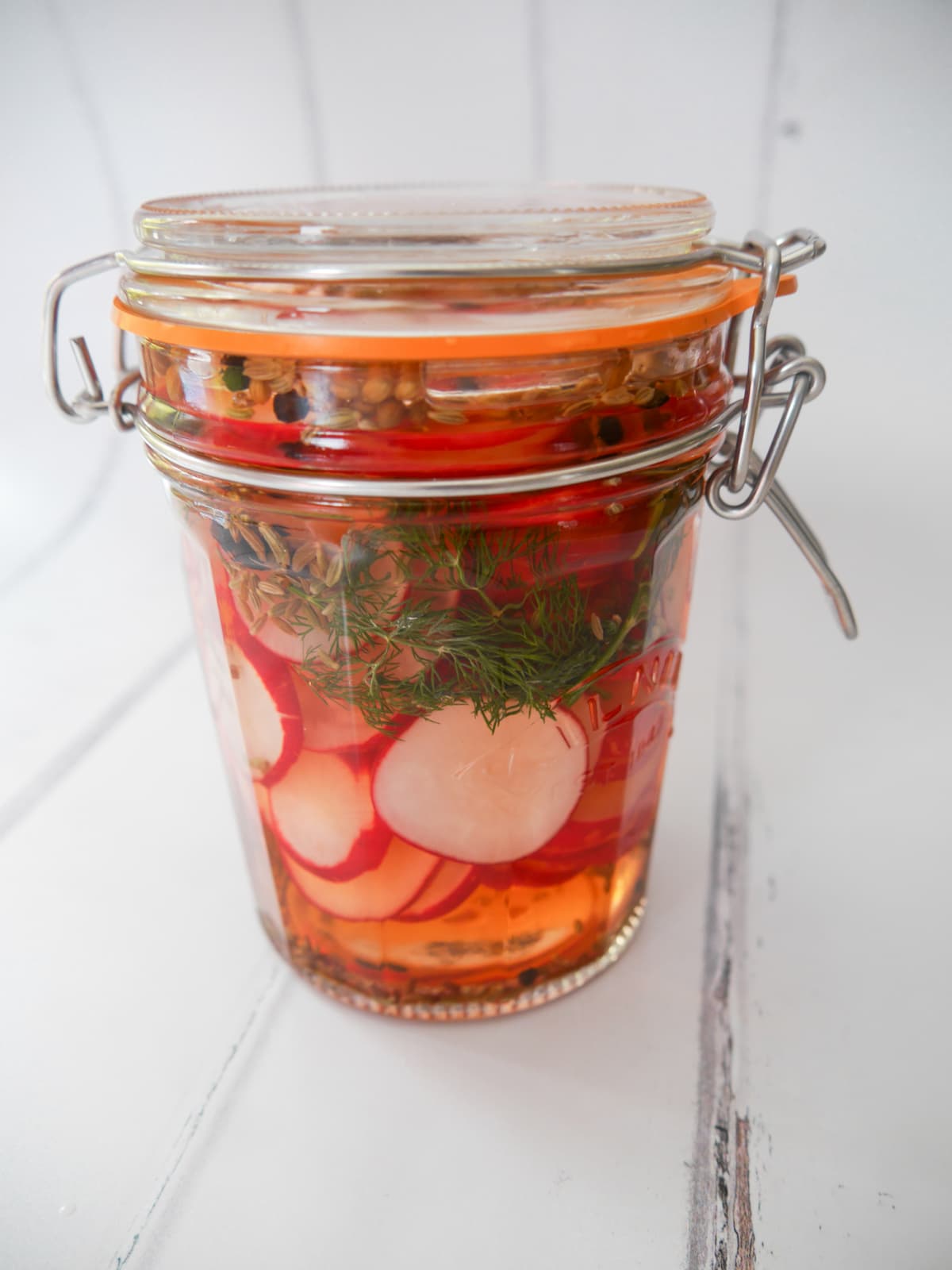 A mason jar filled with pickled radish, dill fronds and whole spices.