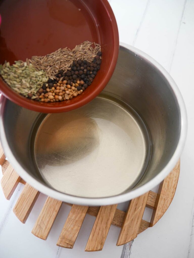 Whole spices being poured into pickling liquid.