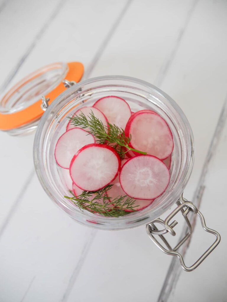 A mason jar filled with sliced radishes and dill fronds.