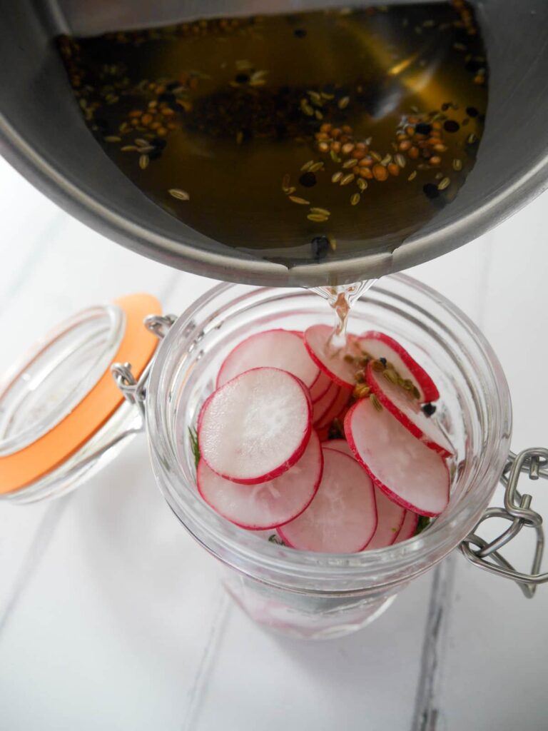 Pickling liquid being poured into a mason jar filled with sliced radishes.