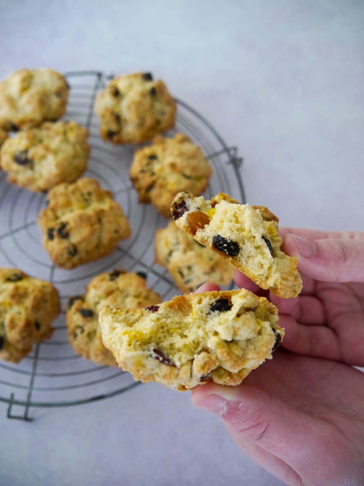 A circular wire rack topped with rock cakes and hands holding a rock cake.