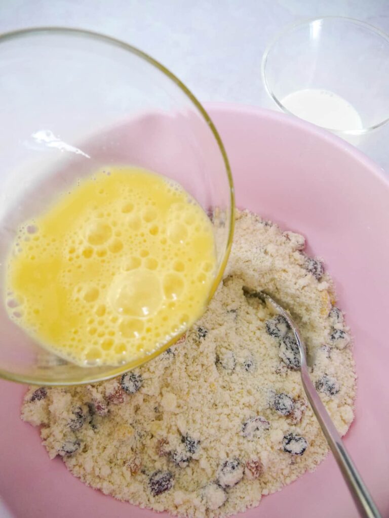Whisked eggs being poured into a bowl of dry rock cake ingredients.