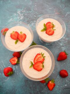 Three individual glass serving dishes filled with strawberry mousse topped with sliced strawberries and mint leaves, with whole strawberries set alongside.