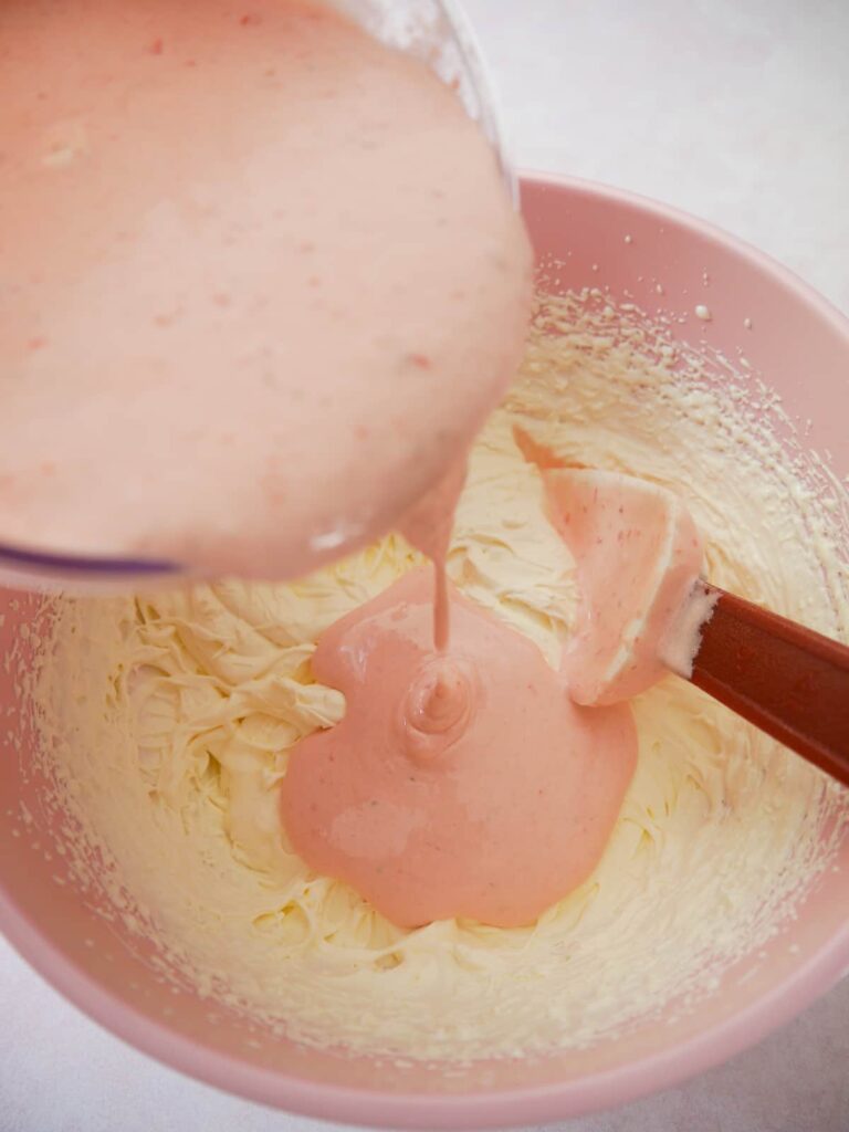 A pink bowl filled with whipped double cream with strawberry meringue mixture being added.