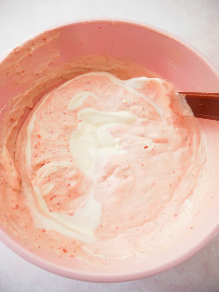 A pink bowl filled with strawberry mousse mixture with Greek yogurt being folded through.