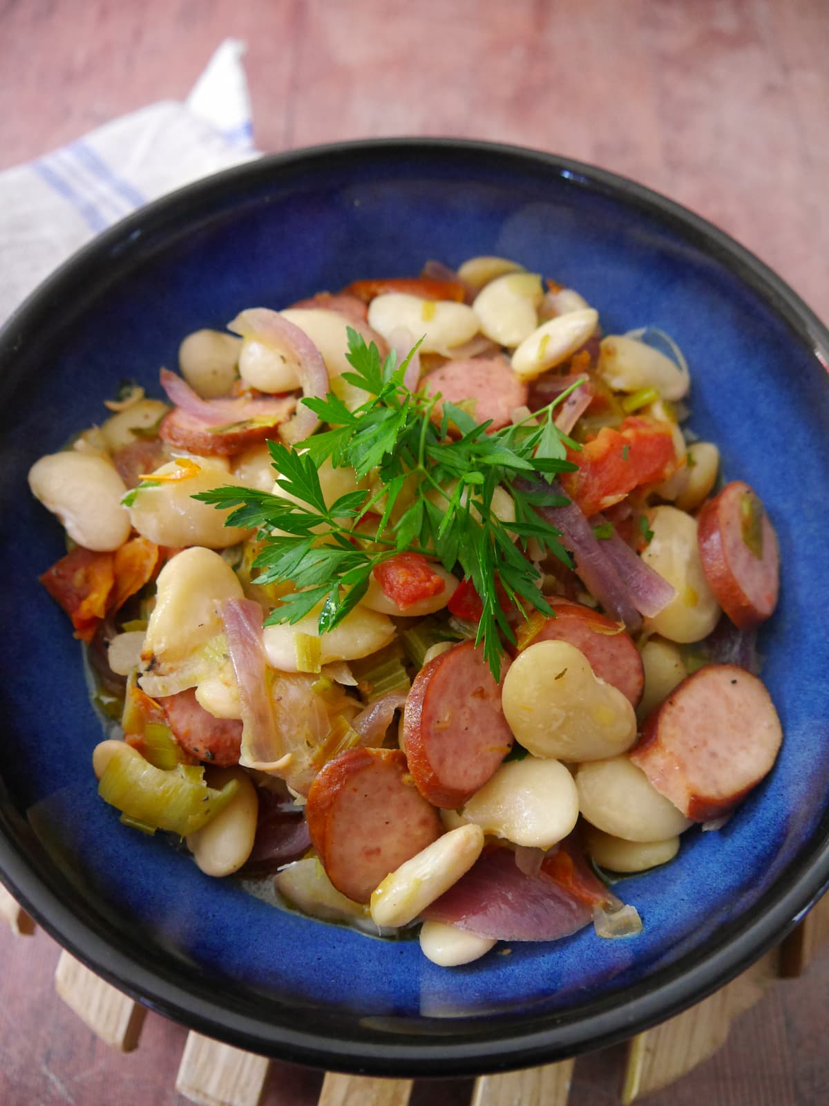 Blue bowl filled with butter bean and smoked sausage stew with a garnish of fresh parsley.
