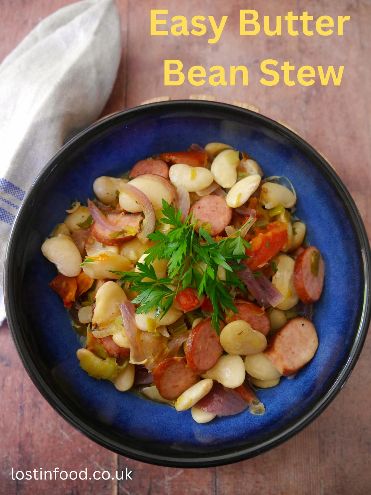 Pinnable image with recipe title and blue bowl filled with butter bean and smoked sausage stew with a garnish of fresh parsley.