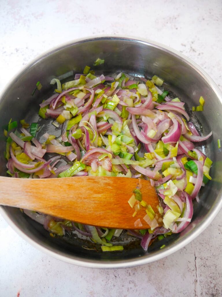 A frying pan of sauteed sliced red onion and leek.