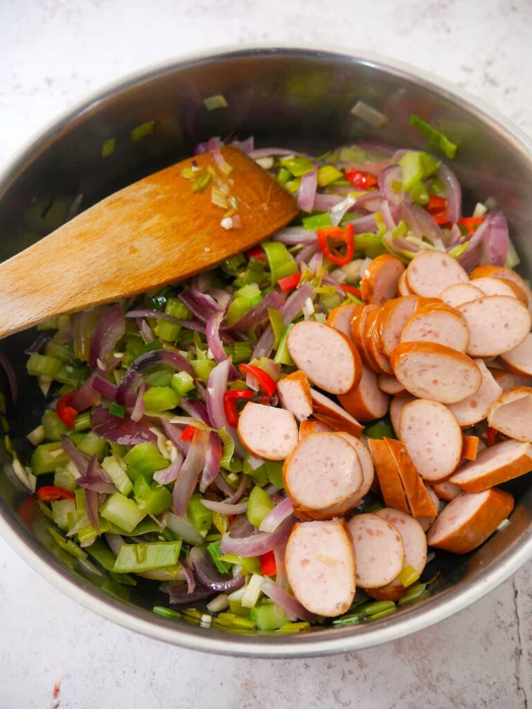 A frying pan of sauteed vegetables with added sliced smoked sausage.