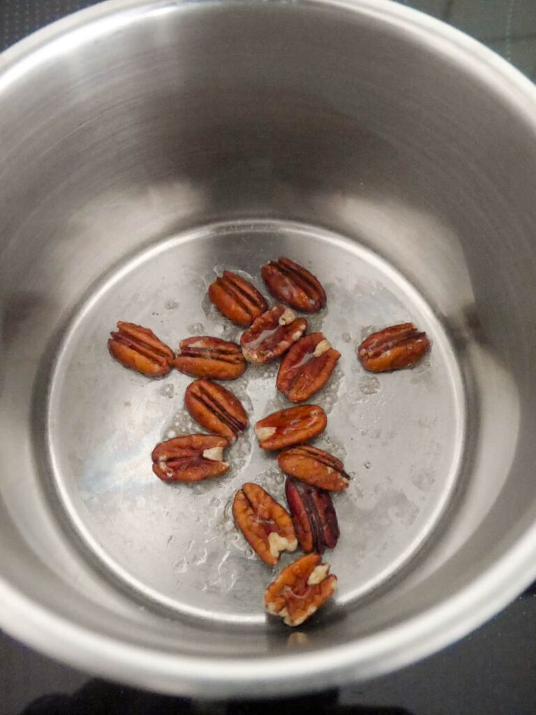 A saucepan with pecans and maple syrup.