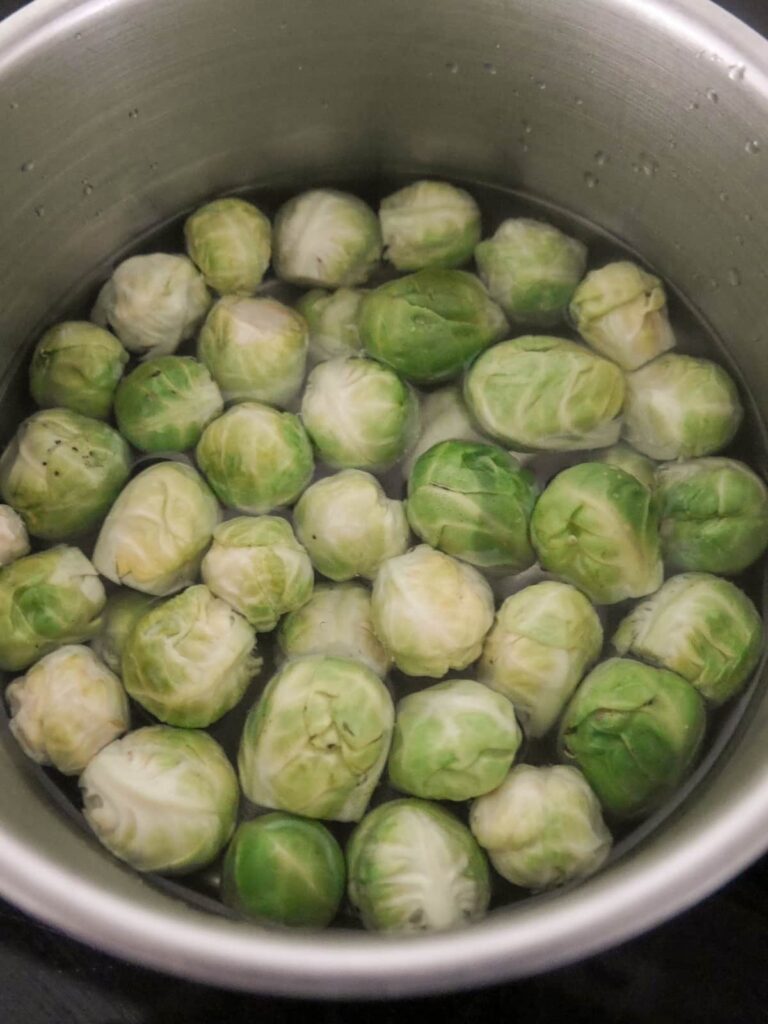 A saucepan filled with water and trimmed Brussels sprouts.