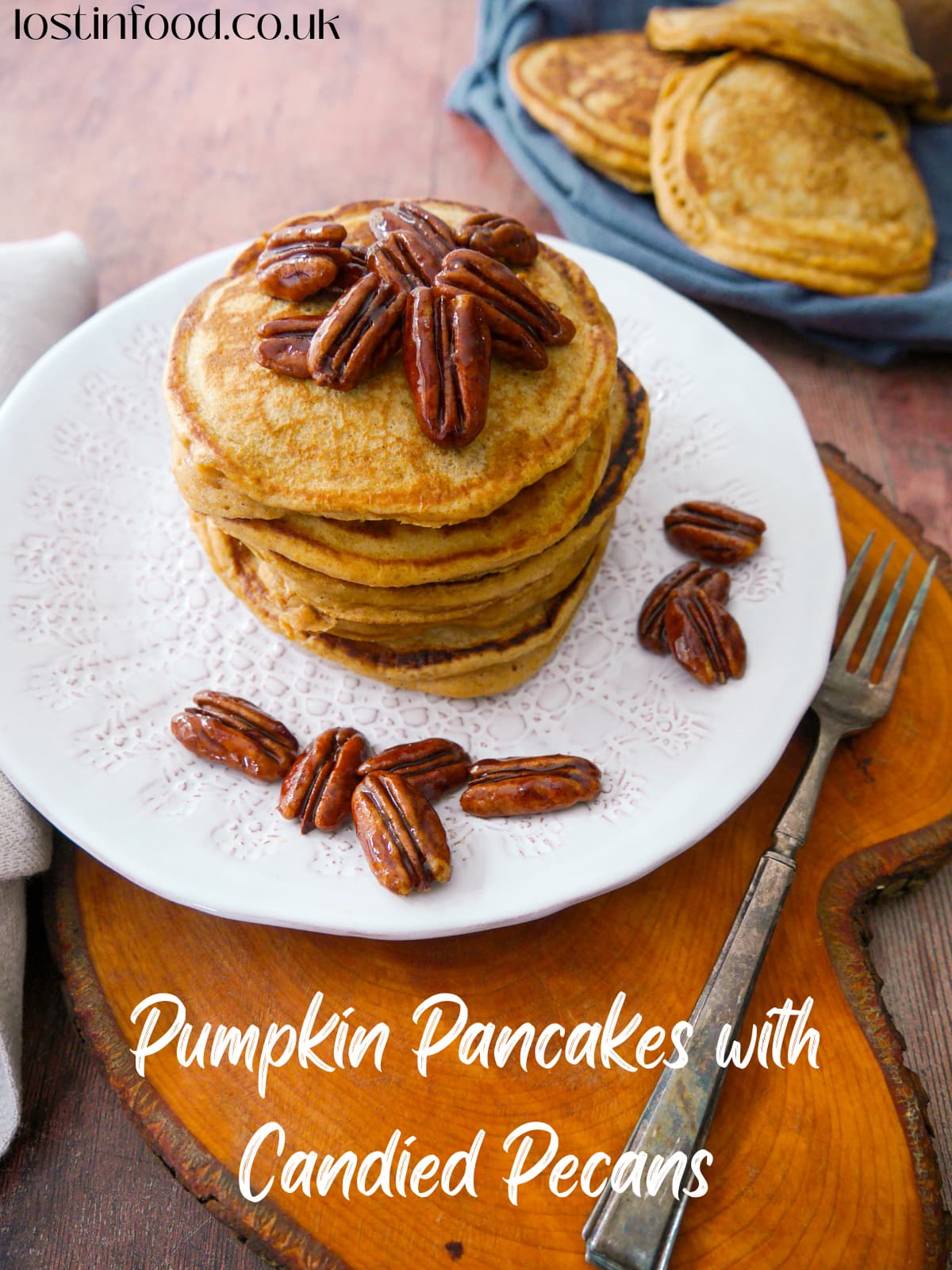 Pinnable image with recipe title and a stack of pumpkin pancakes on a white plate, topped with candied pecans and maple syrup, with a plate of pumpkin pancakes set alongside.
