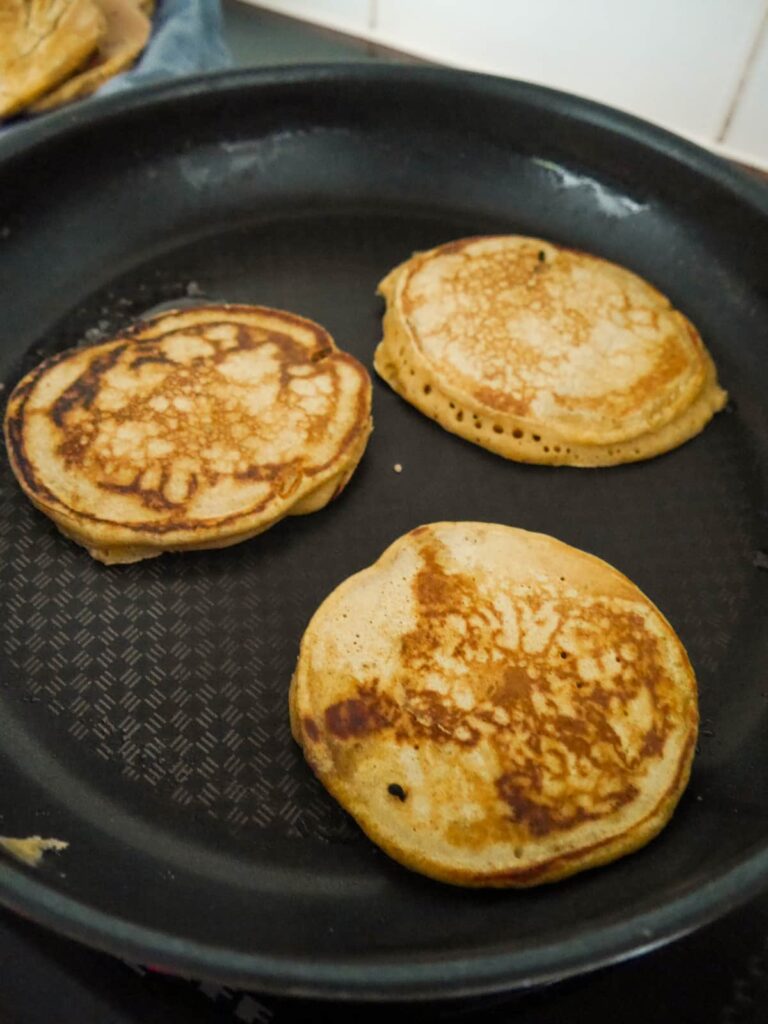 A non stick pan with 3 cooked pumpkin pancakes.