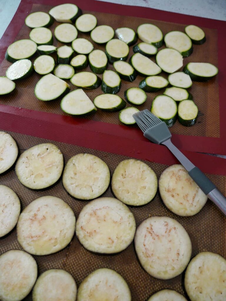 Two trays topped with a silicone liners with slices of aubergine and courgette set on top.