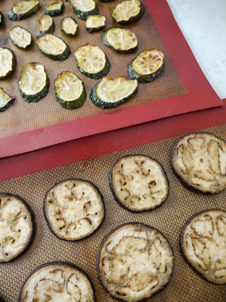 Two trays topped with a silicone liners with slices of roasted aubergine and courgette set on top.