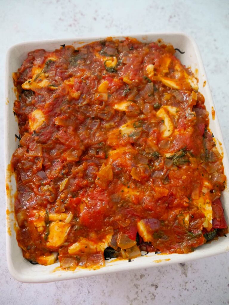 A dish of layered vegetables and mozzarella cheese topped with tomato and basil sauce.