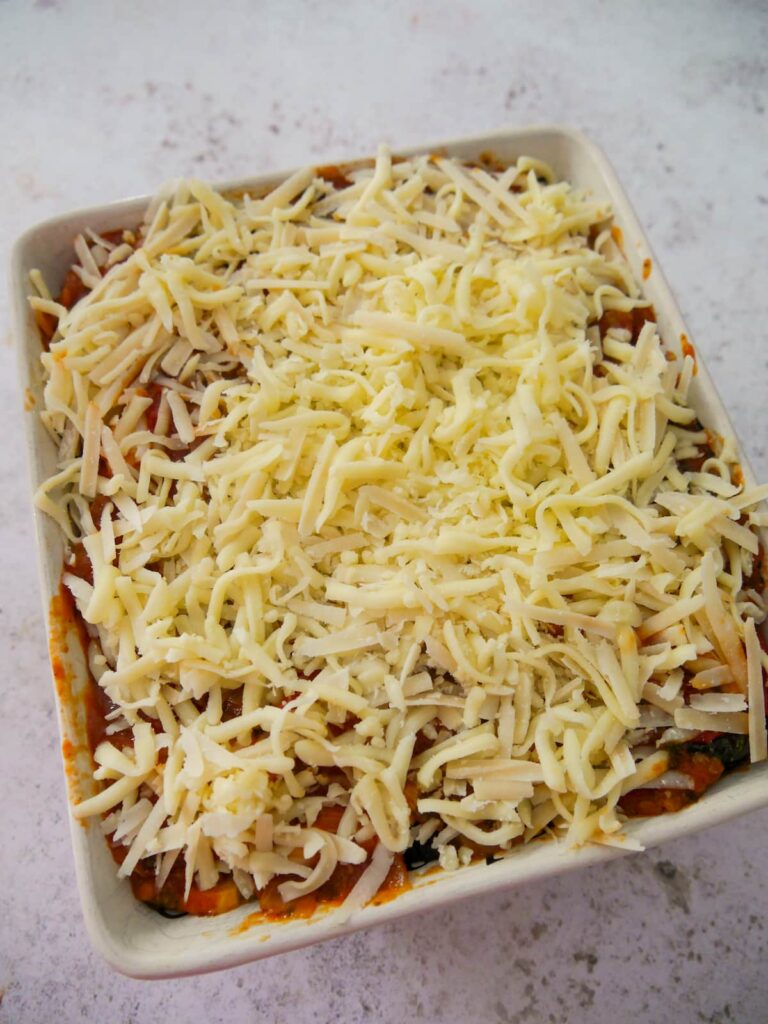 A dish of roasted vegetable bake topped with shredded cheese.