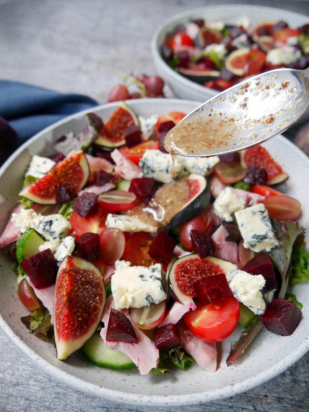 Red wine vinagrette dressing being poured over a bowl of ham salad with figs and blue cheese.