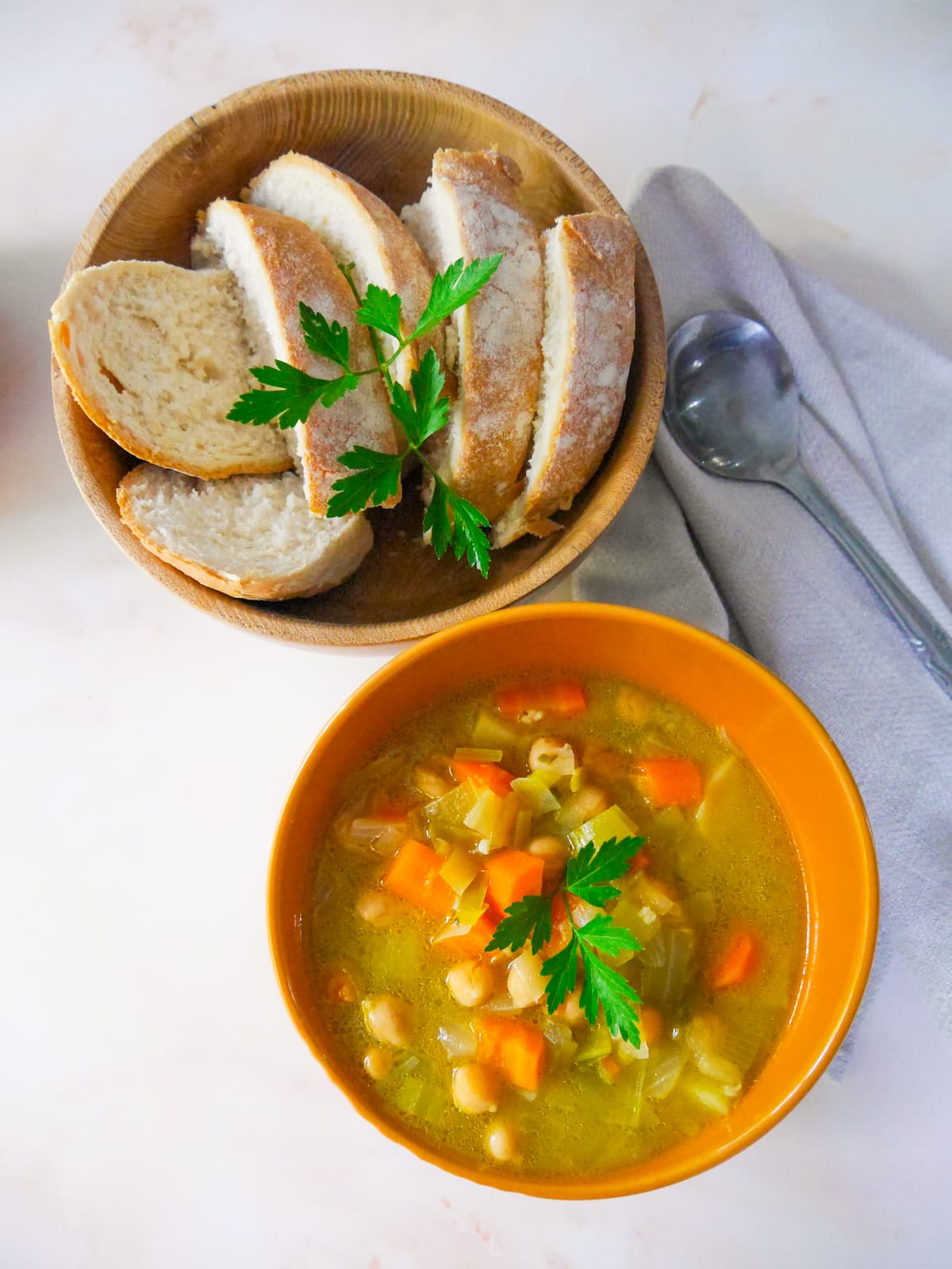 A bowl of leek, potato and chickpea soup with a bowl of sliced bread set alongside.