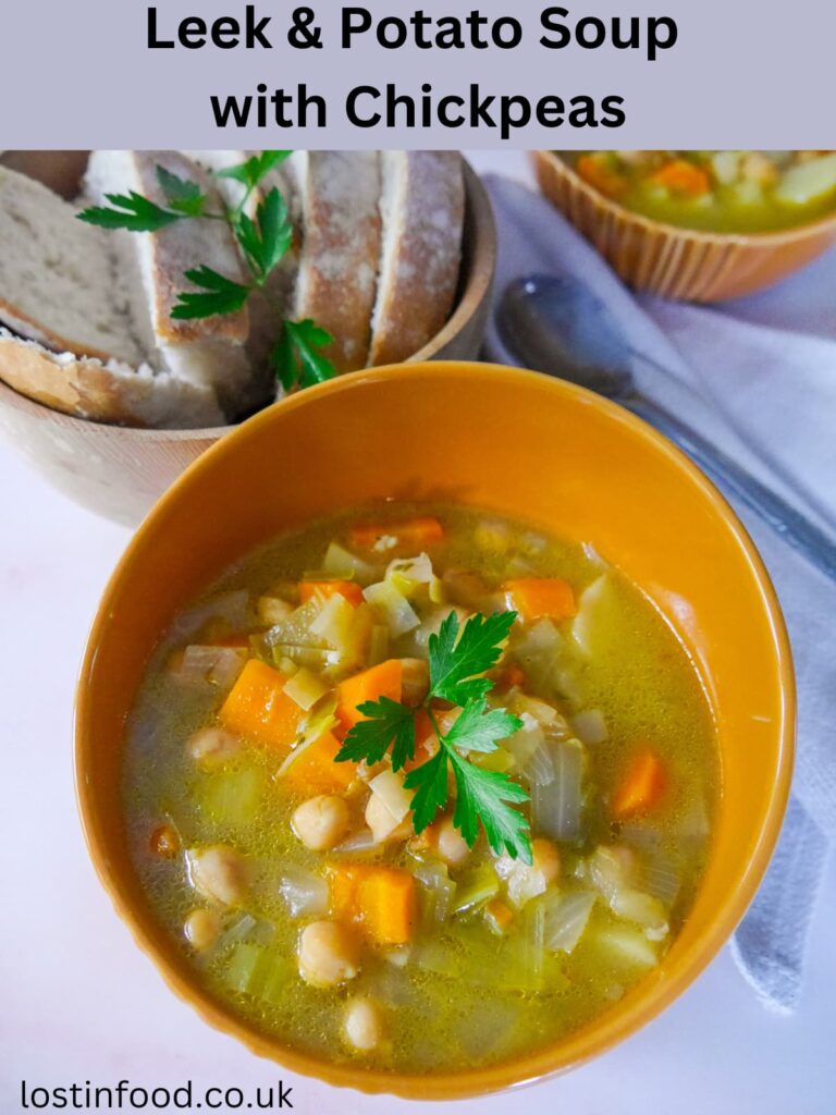 Pinnable image with recipe title and a bowl of leek, potato and chickpea soup with a bowl of sliced bread set alongside.