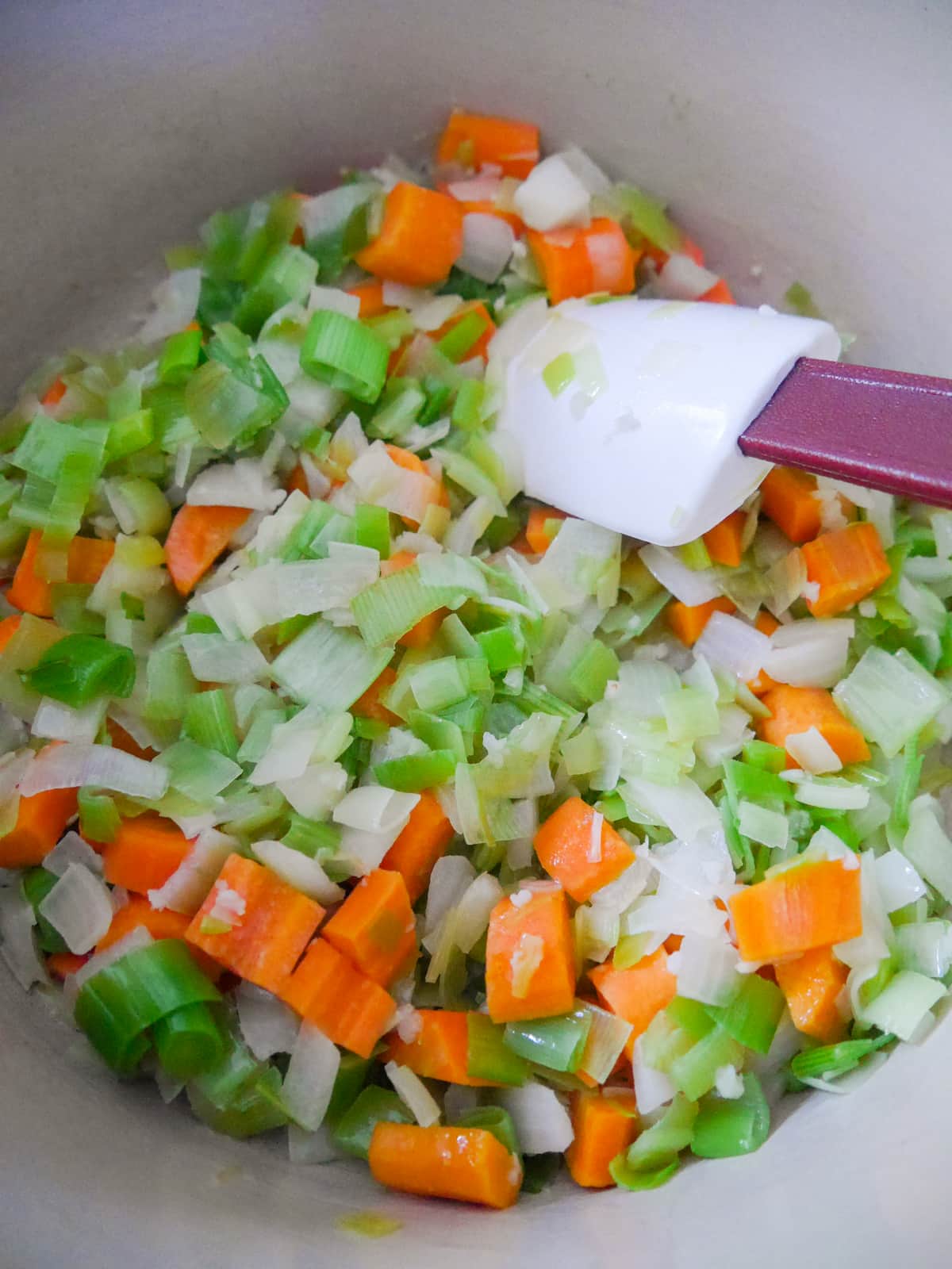 A large pan filled with sauteed leek, onion, carrot and garlic.