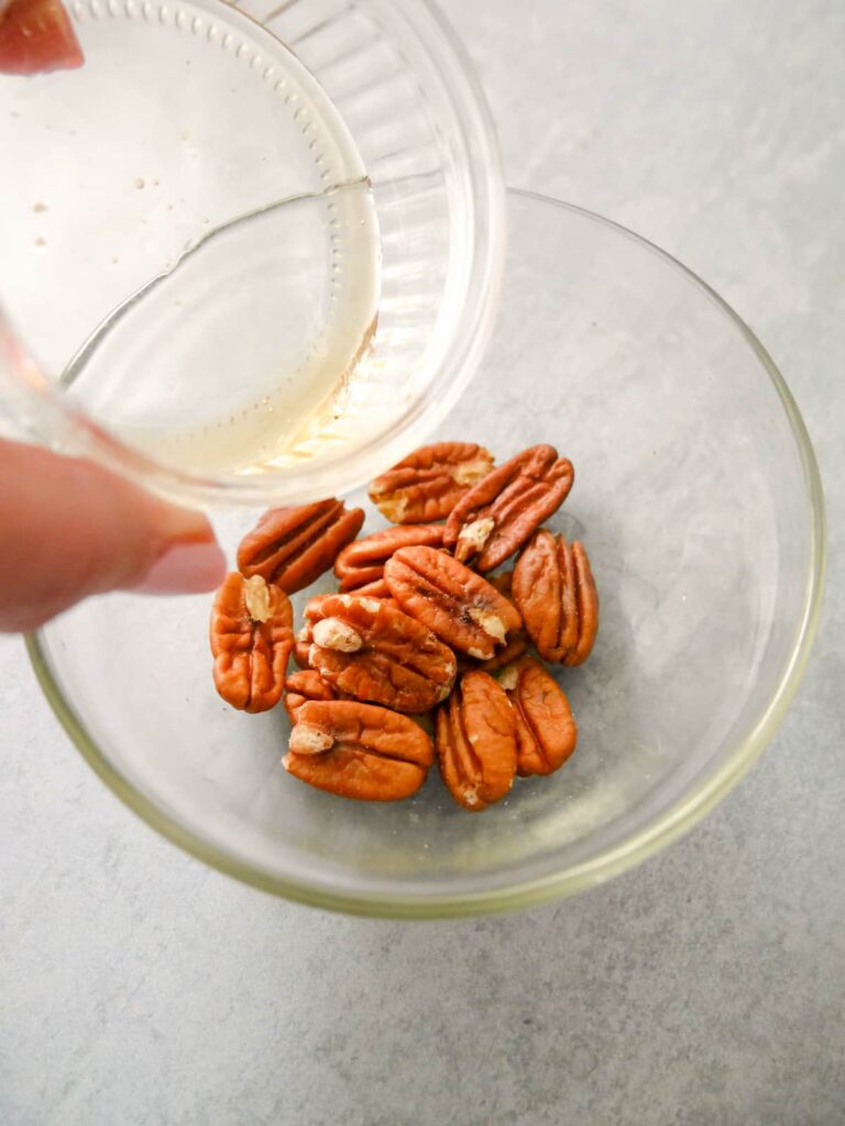 A jar filled with whole pecans with honey being poured over.