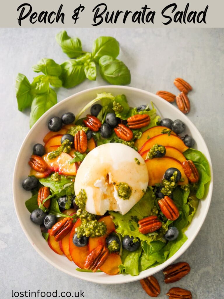 Pinnable image with recipe title and a bowl of peach and burrata salad with blueberries, candied pecans and basil pesto.