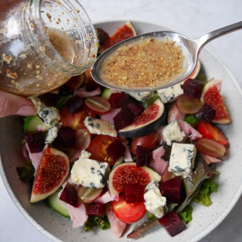 Red wine vinaigrette being spooned over a ham, fig and blue cheese salad.